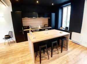 Cuisine rénovée avec îlot central en bois, placards noirs, électroménager moderne et plancher en bois clair.